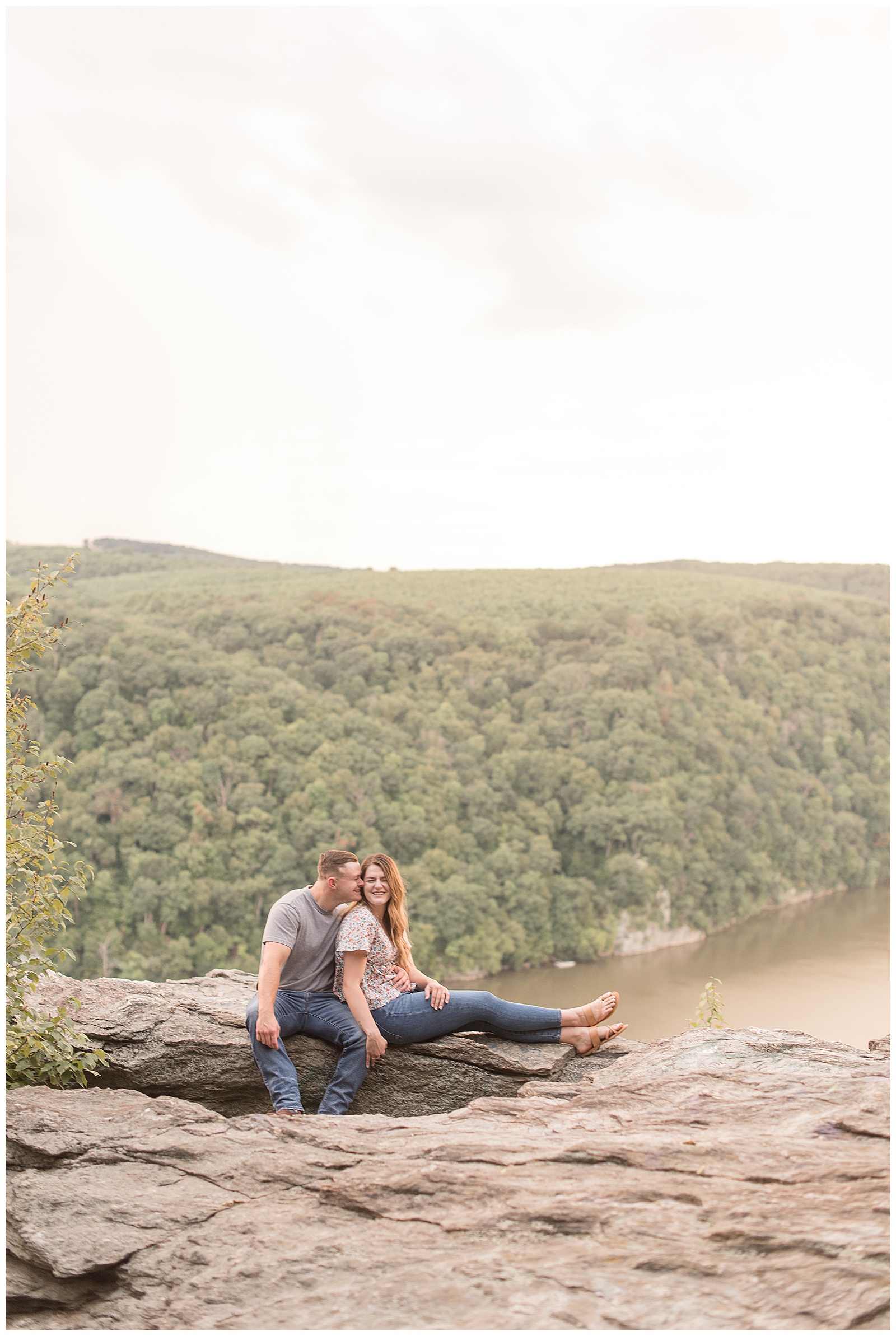 engaged couple sitting on large rock as guy snuggles against girl at pinnacle overlook