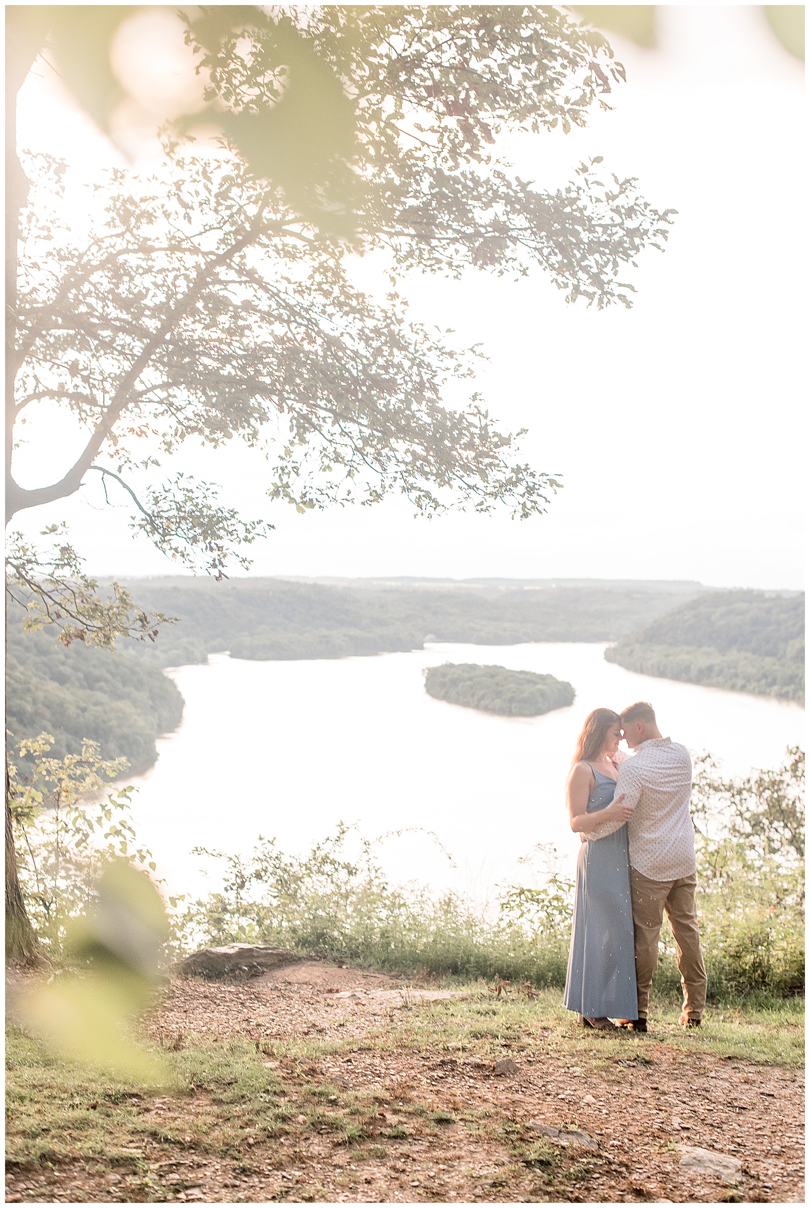 engaged couple hugging atop pinnacle overlook with girl in long light blue dress and guy wearing white patterned dress shirt and khaki pants 