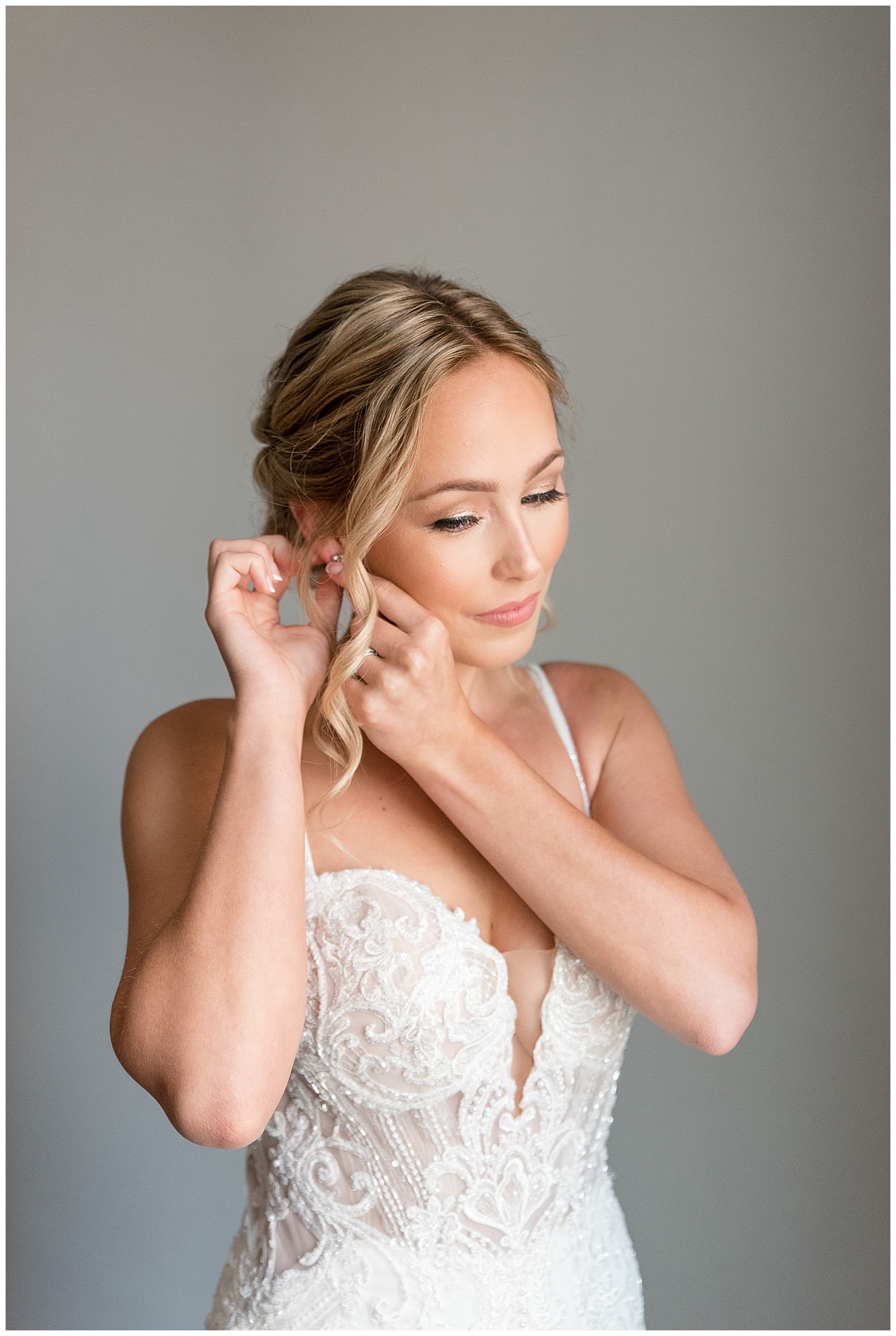 bride adjusts her earring looking down and wearing gorgeous modern wedding gown in lancaster pennsylvania