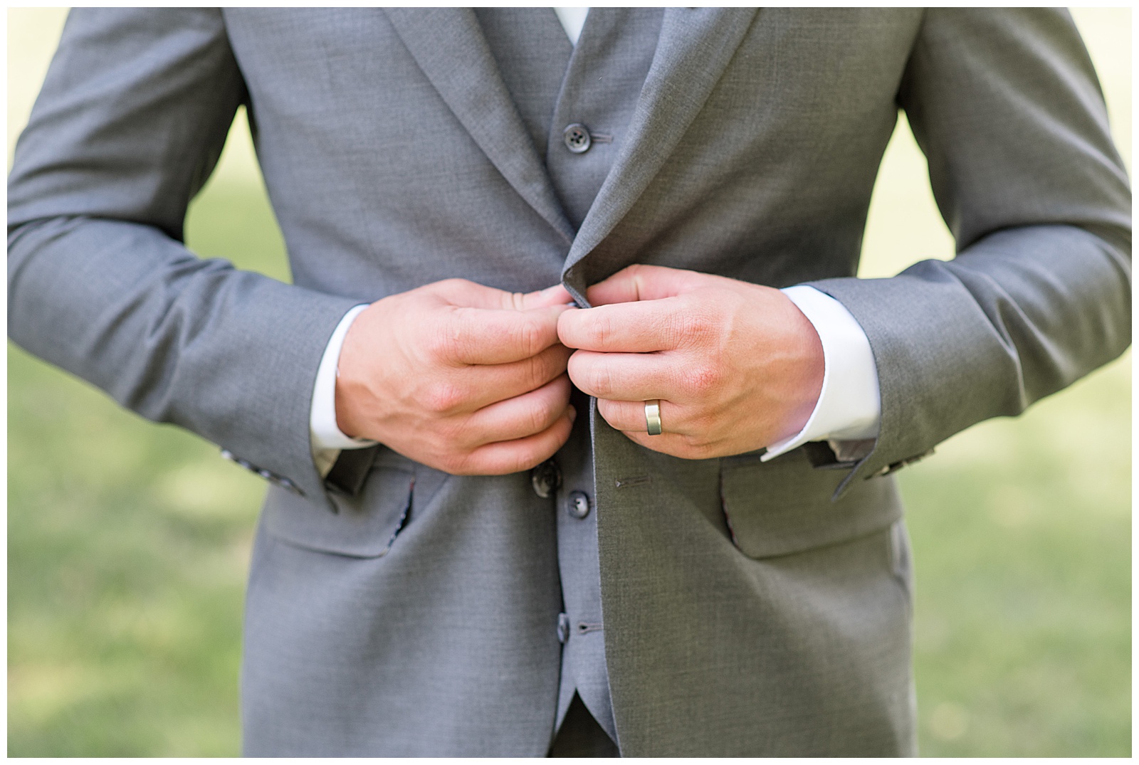 closeup photo of groom buttoning his gray suit coat with white dress shirt at the barn at silverstone