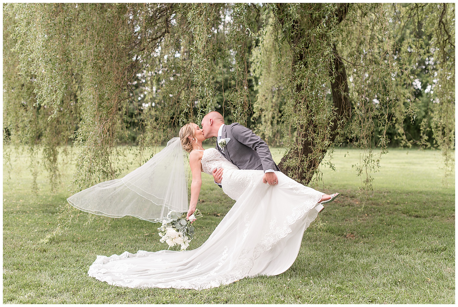 groom dips bride back kissing her under willow tree at the barn at silverstone