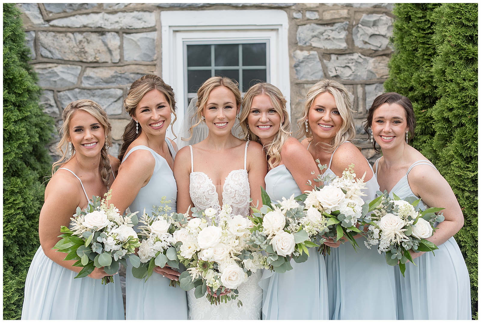 bride and bridesmaids holding beautiful bouquets all smiling at camera in front of stone building at the barn at silverstone