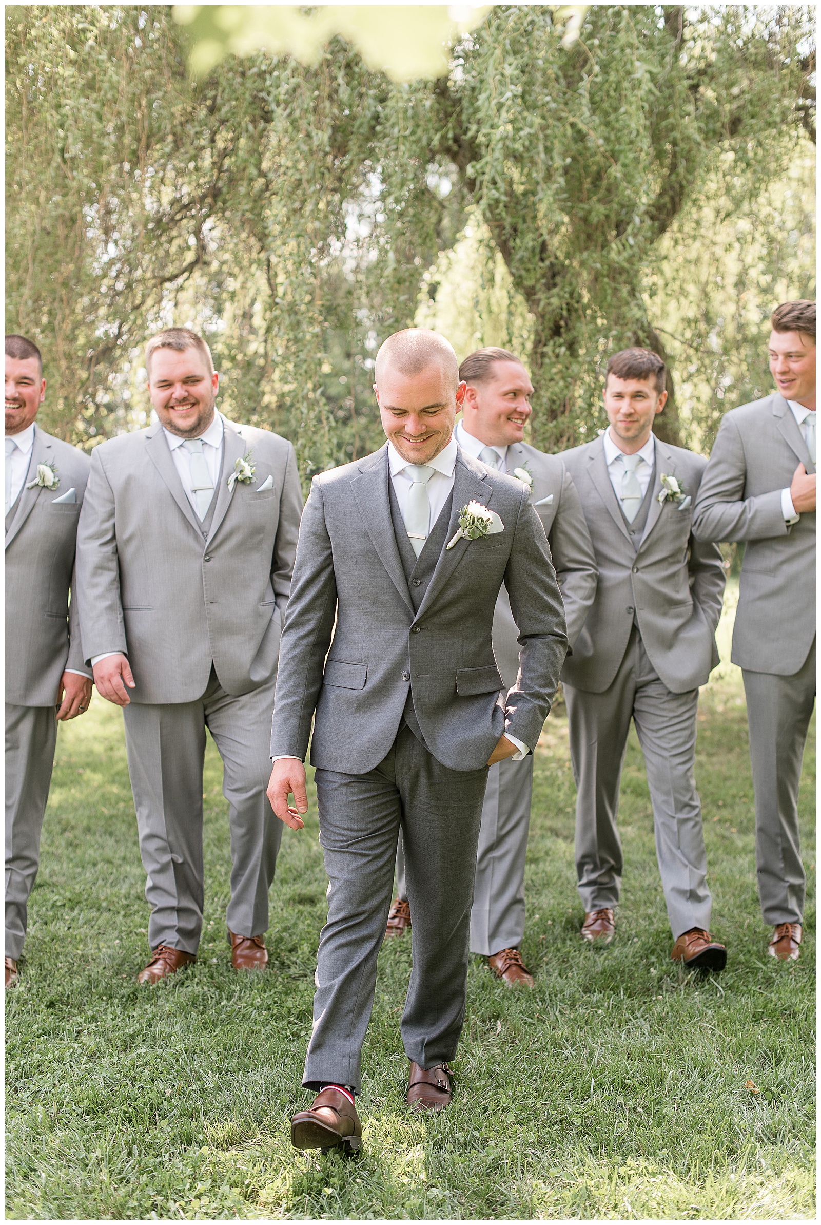 groom walking ahead of groomsmen as they all look in different directions smiling at the barn at silverstone