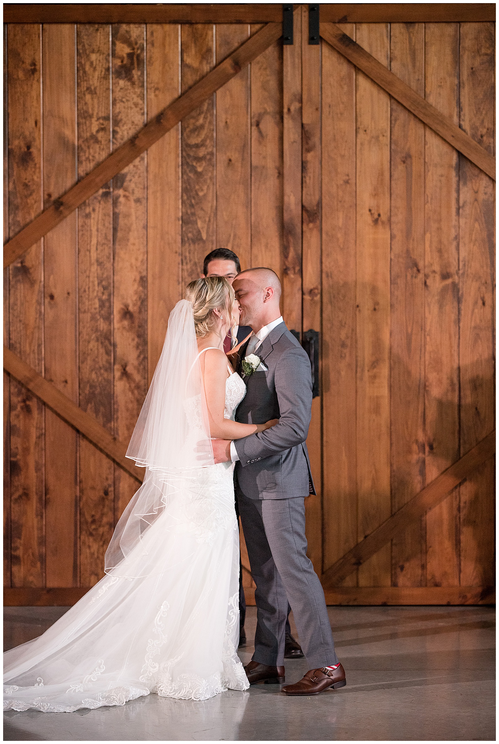 bride and groom kissing for the first time during wedding ceremony inside beautiful barn at the barn at silverstone