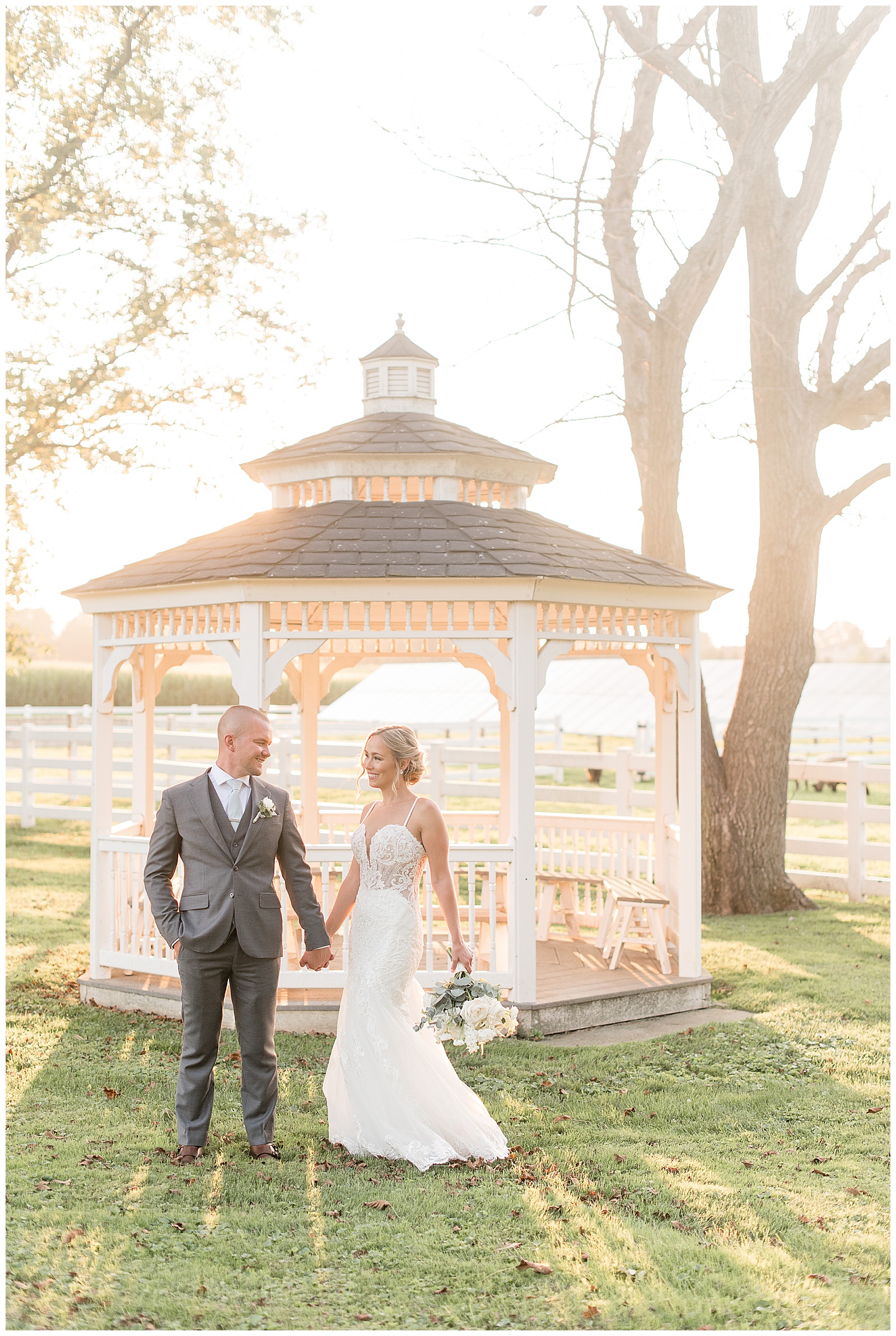 bride and groom holding hands in front of cute white gazebo on bright sunny evening at the barn at silverstone