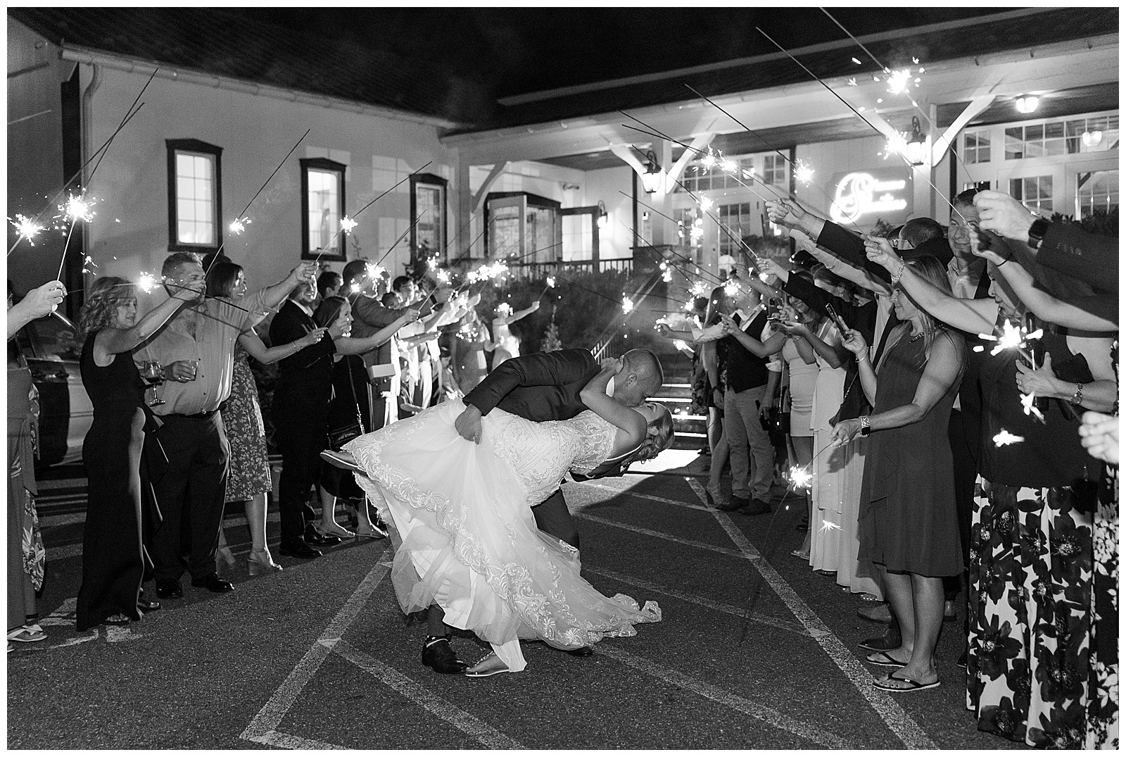 groom kissing bride as he dips her back outside barn reception during sparkler send off surrounded by wedding guests in lancaster pennsylvania