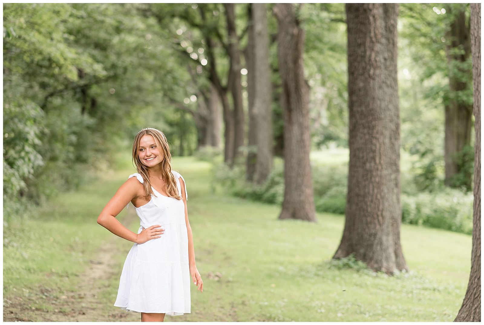 senior girl in white dress with right hand on hip looking over right shoulder smiling at lancaster county park
