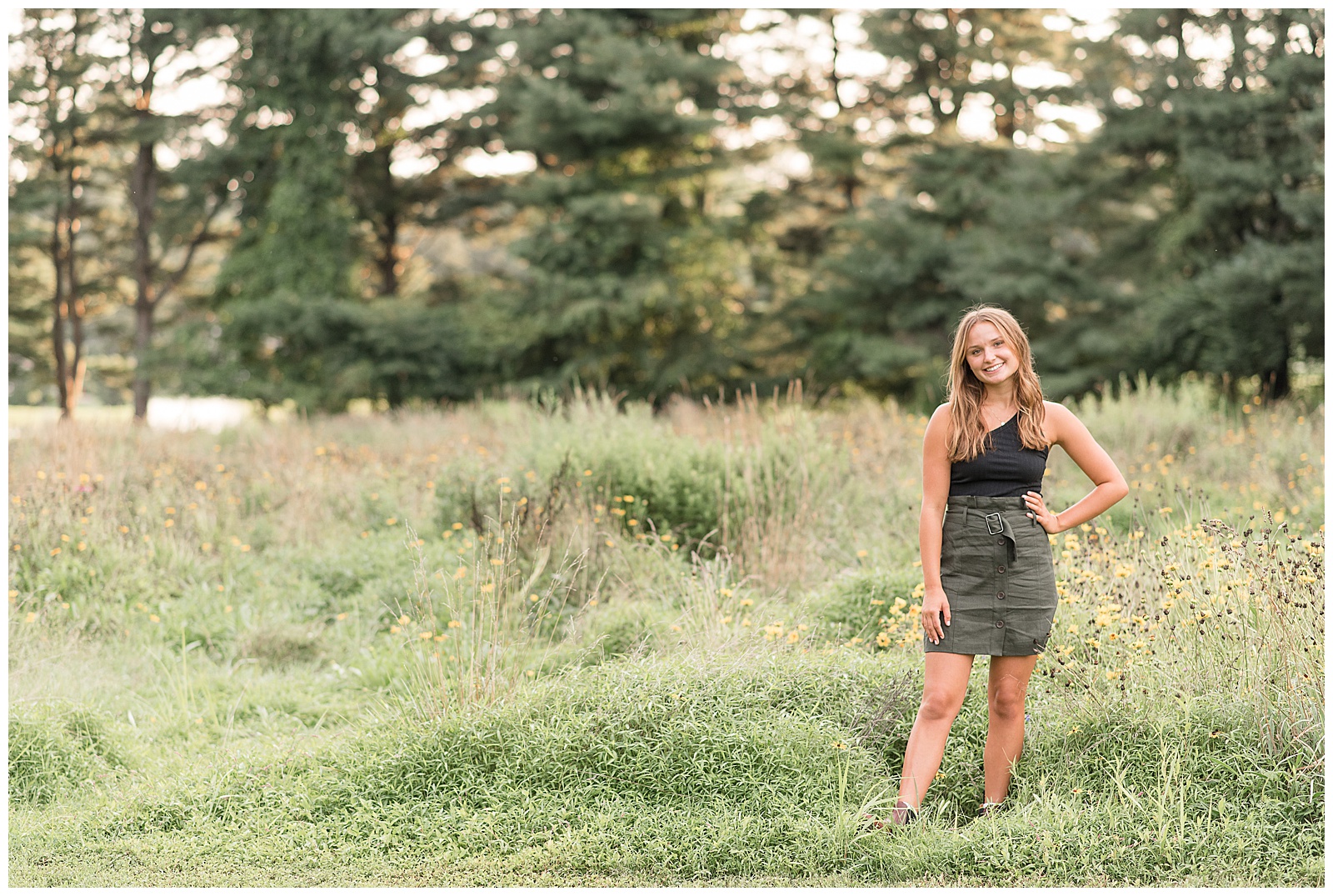 senior girl smiling with left hand on hip by tall grasses at park in lancaster, pennsylvania