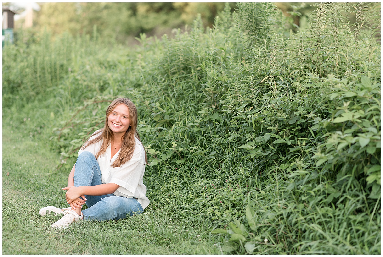 senior girl sitting in grass next to tall wild grasses on sunny summer evening in lancaster county park