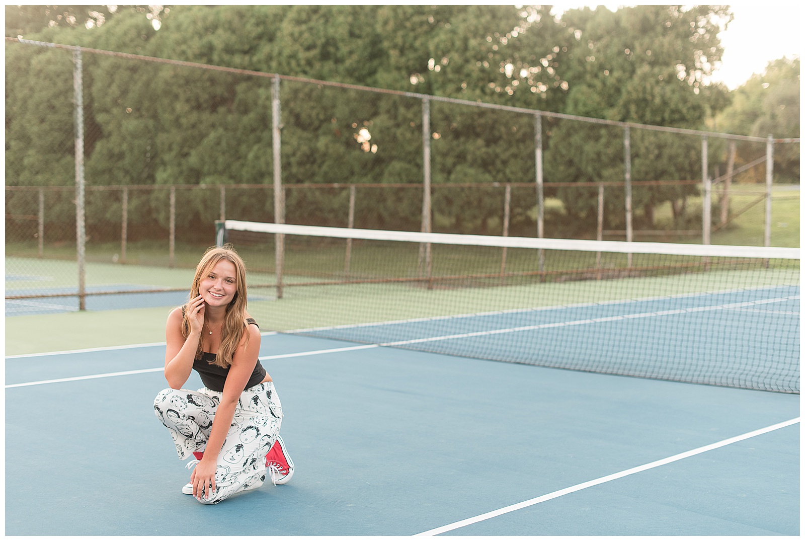 senior girl in black midi tank top and printed pants crouching down on blue tennis court at lancaster county park