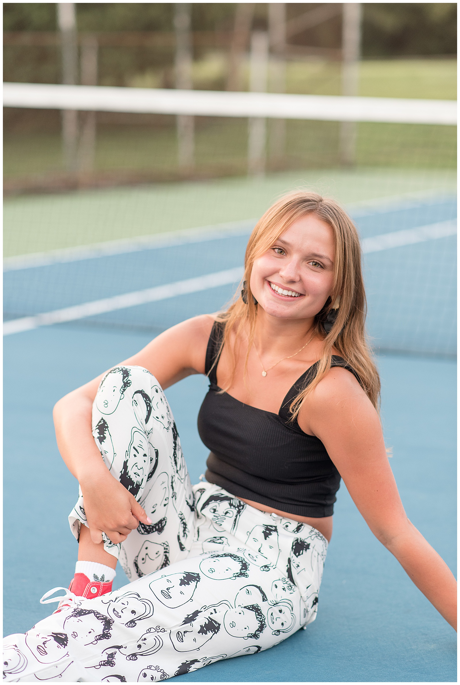 senior girl sitting on blue tennis court with right knee bent and left arm holding her up at lancaster county park