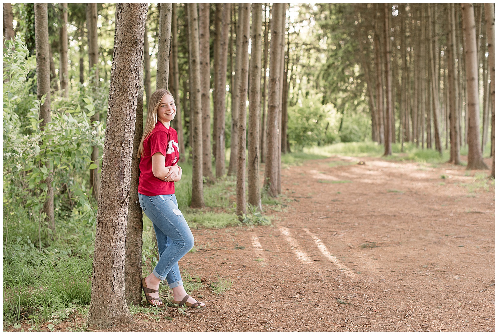 senior girl leaning against pine tree with right leg bent and propped against tree at overlook park