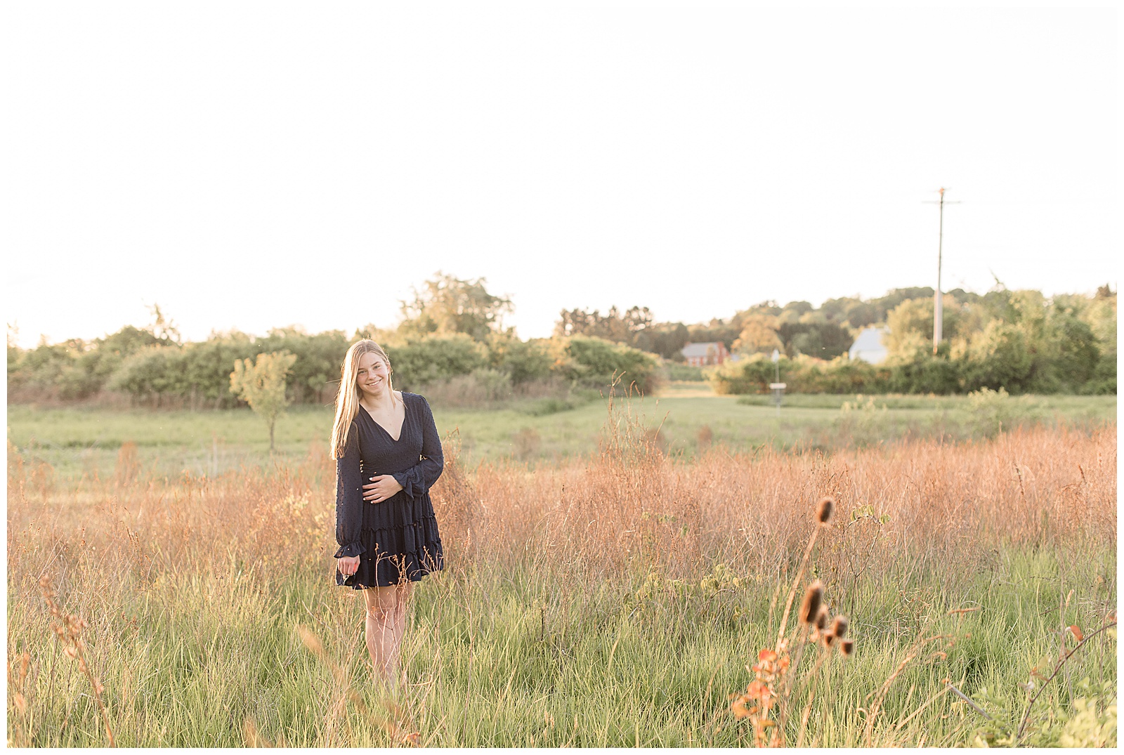 senior girl standing in wildflower field with arms crossed on sunny summer evening at overlook park in lancaster pennsylvania
