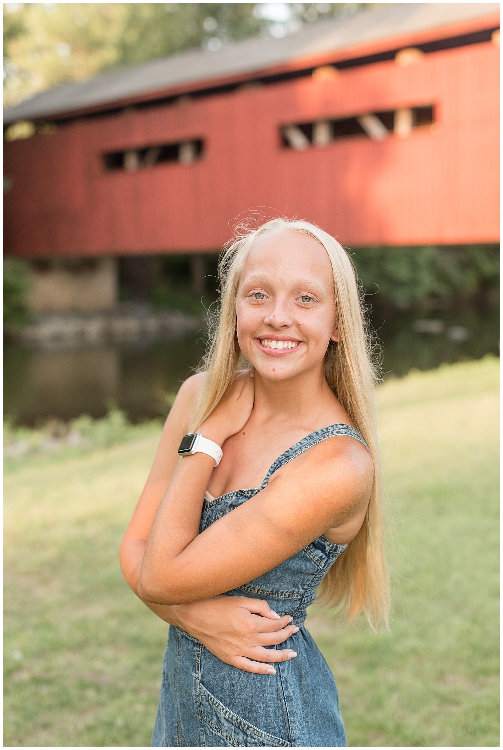 closeup photo of senior girl smiling with left hand on right shoulder and red covered bridge behind her in mechanicsburg pennsylvania