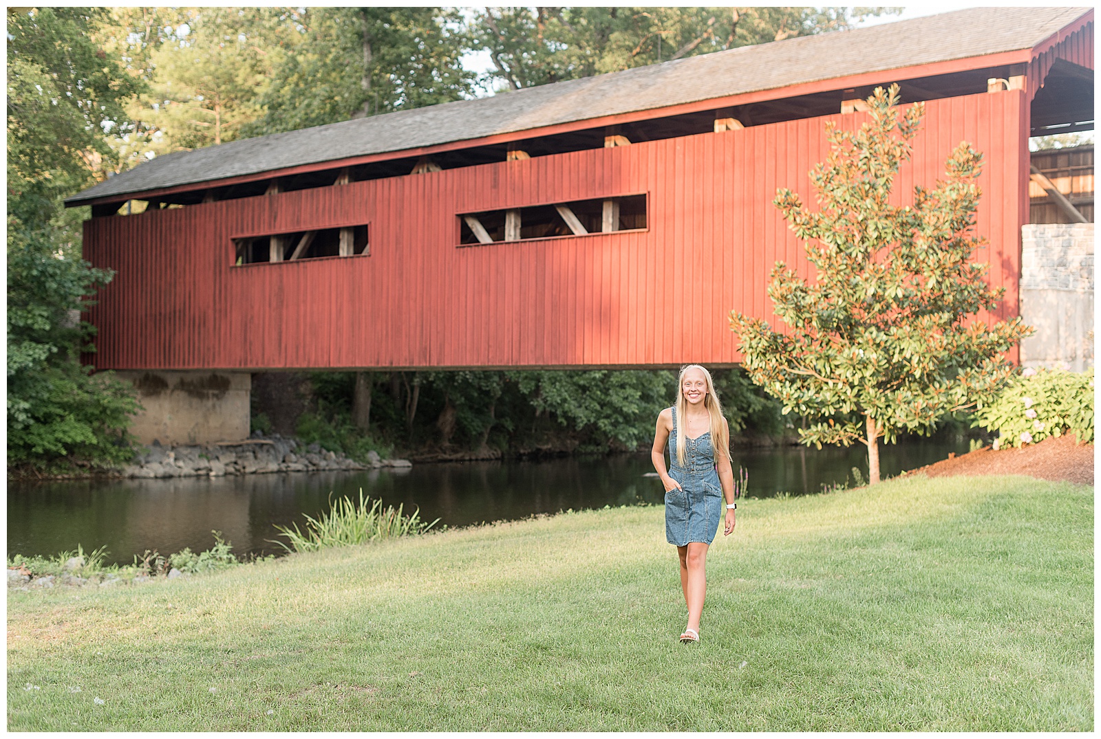 senior girl walking towards camera with right hand on hip by red covered bridge at messiah university