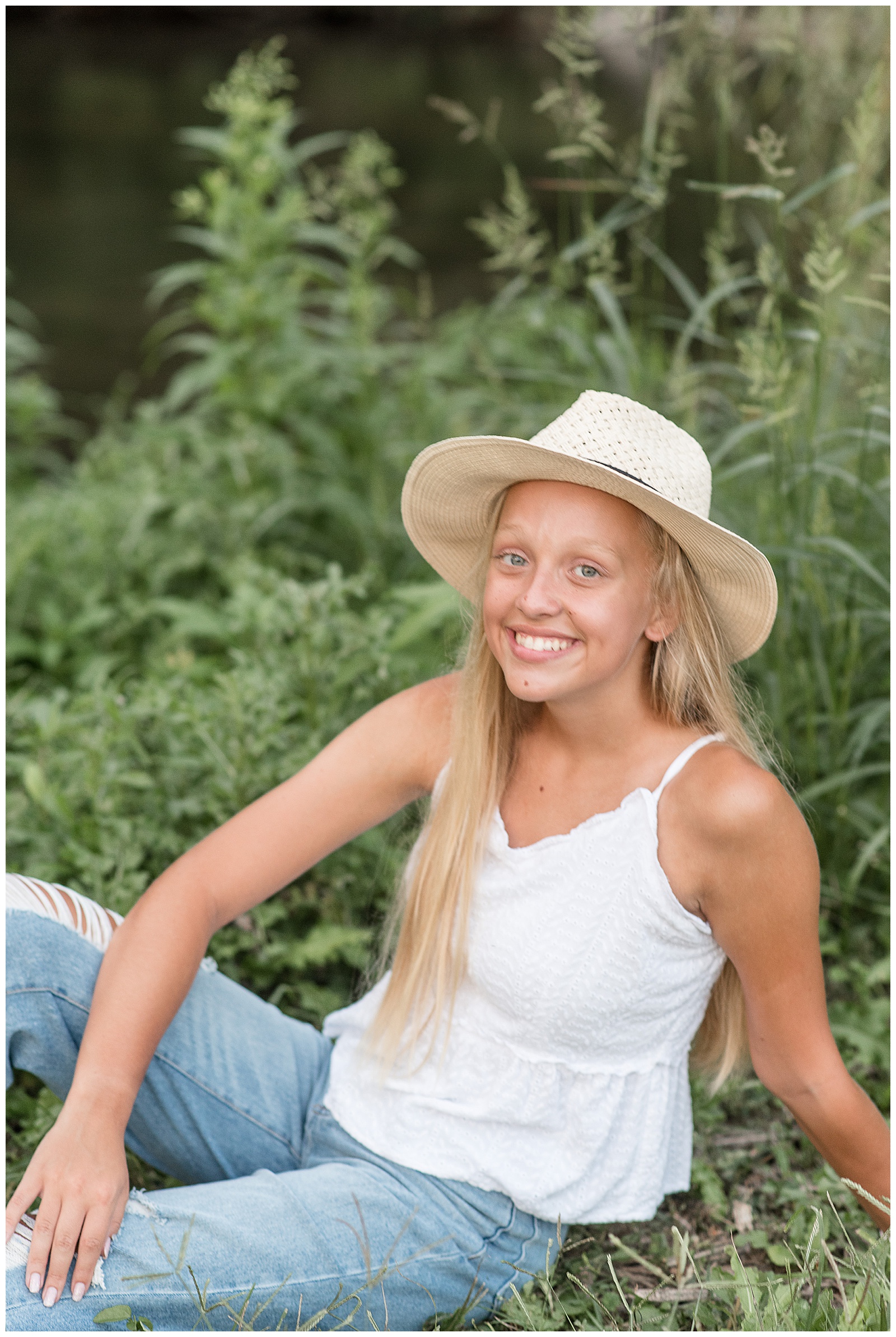 closeup photo of senior girl sitting in grass smiling wearing cute hat with green plants behind her in mechanicsburg pennsylvania