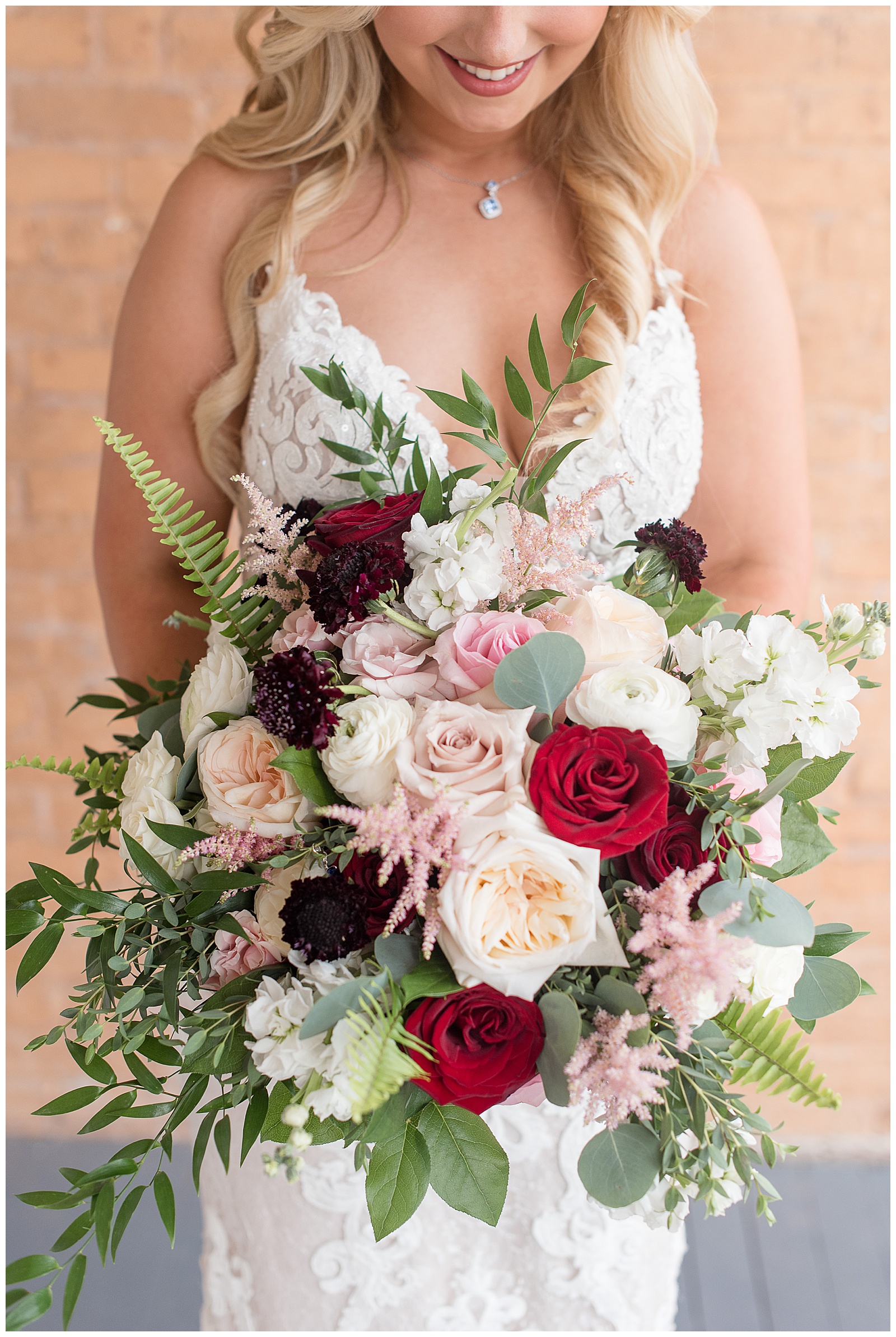 closeup photo of bride holding bouquet filled with ivory, light pink, and maroon roses and greenery at Antrim 1844