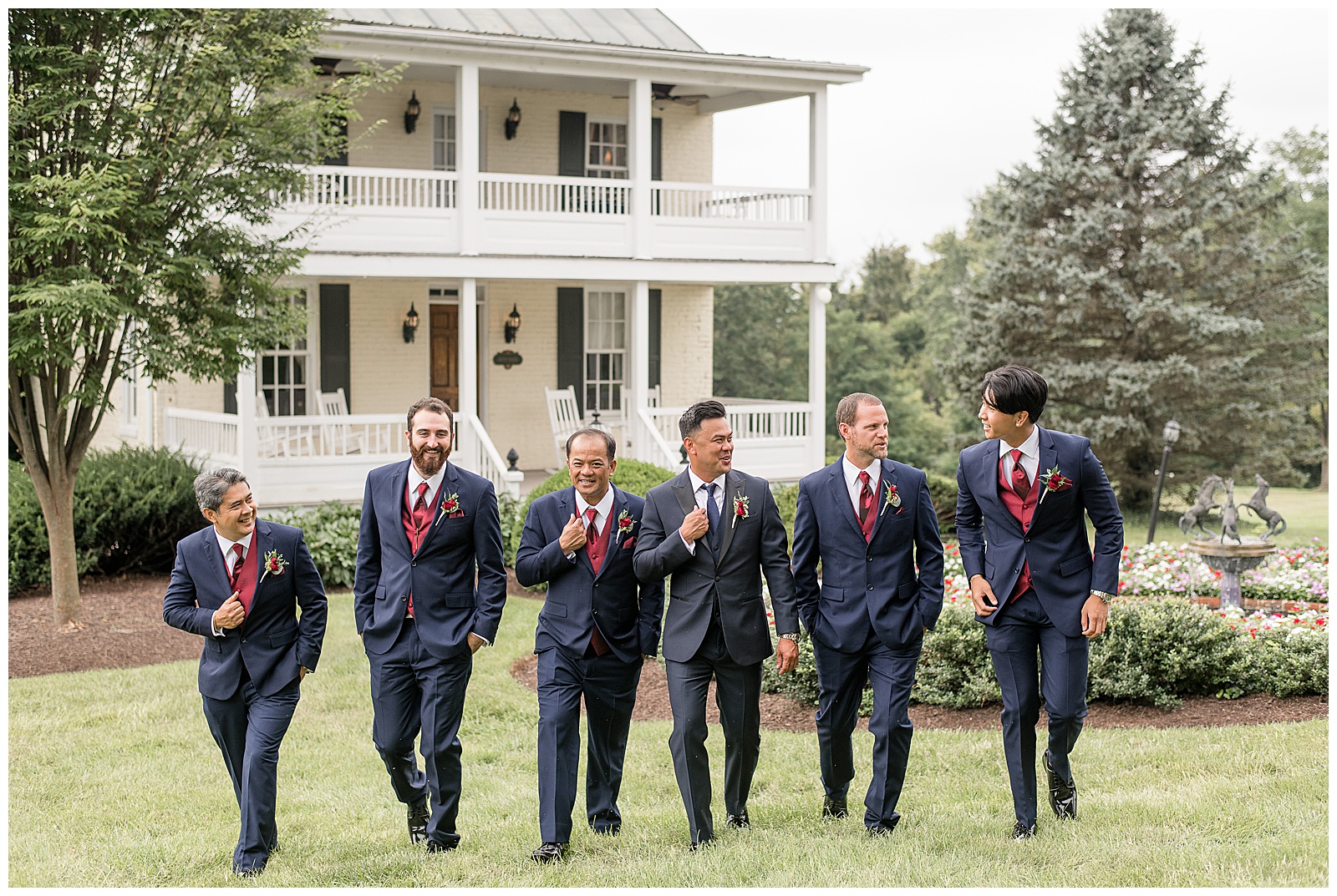 groom and five groomsmen wearing navy blue suits with maroon ties walking towards camera outside Antrim 1844 on grass yard