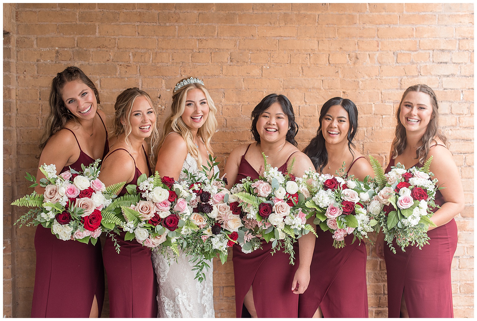 bride with five bridesmaids wearing maroon spaghetti strap gowns standing along brick wall in maryland