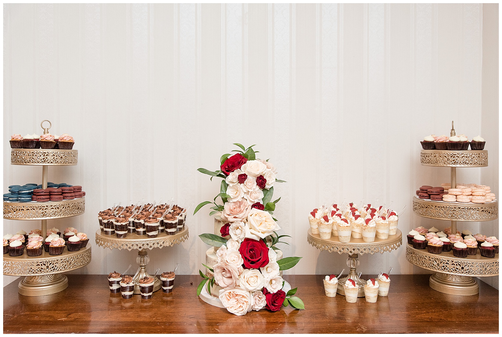 beautiful wedding cake and cupcakes displayed on wooden table by white wall at Antrim 1844