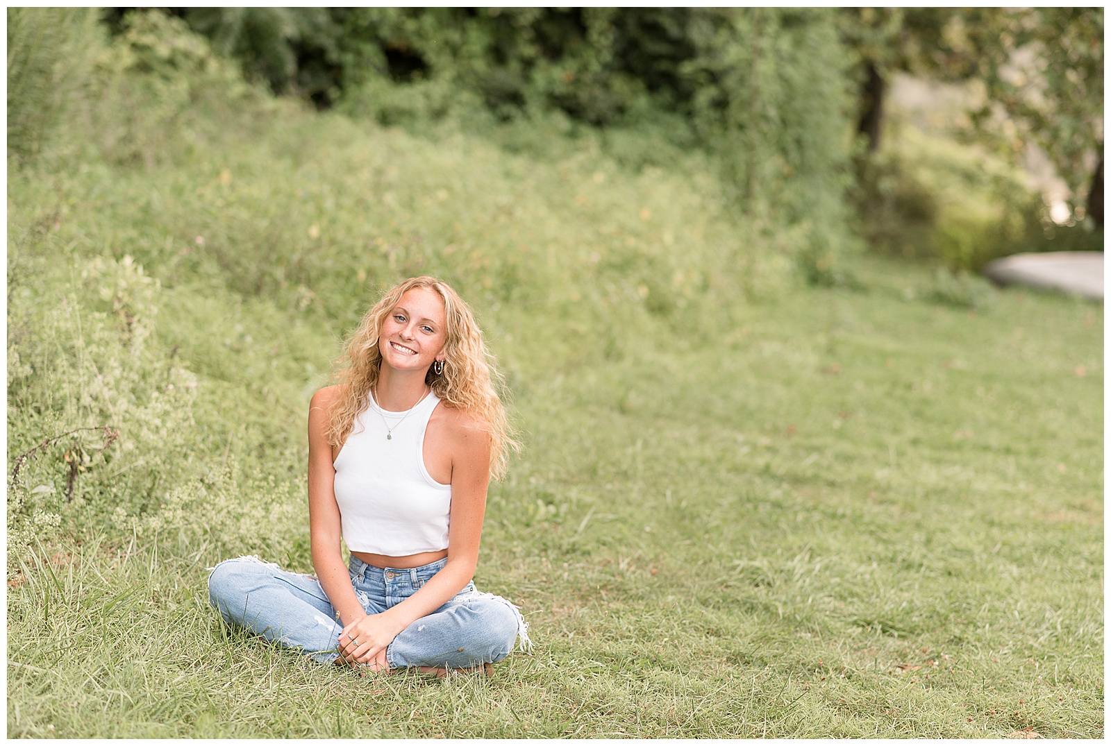 senior girl sitting in grass smiling by tall grasses at speedwell forge lake in lititz pennsylvania