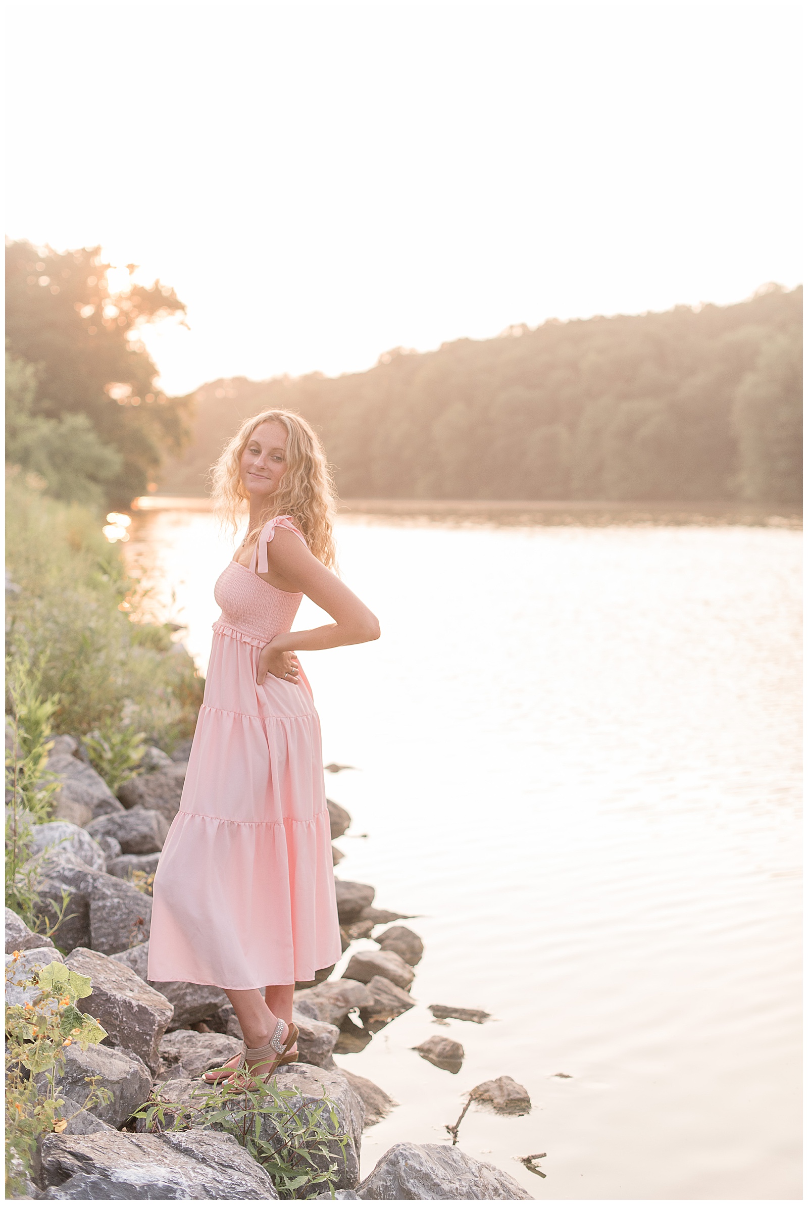 senior girl on large rocks by speedwell forge lake as the bright sun sets behind her in lititz pennsylvania
