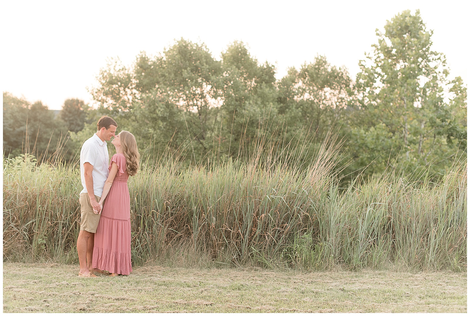 engaged couple holding hands and standing close on left side of photo next to tall grasses in lancaster pennsylvania