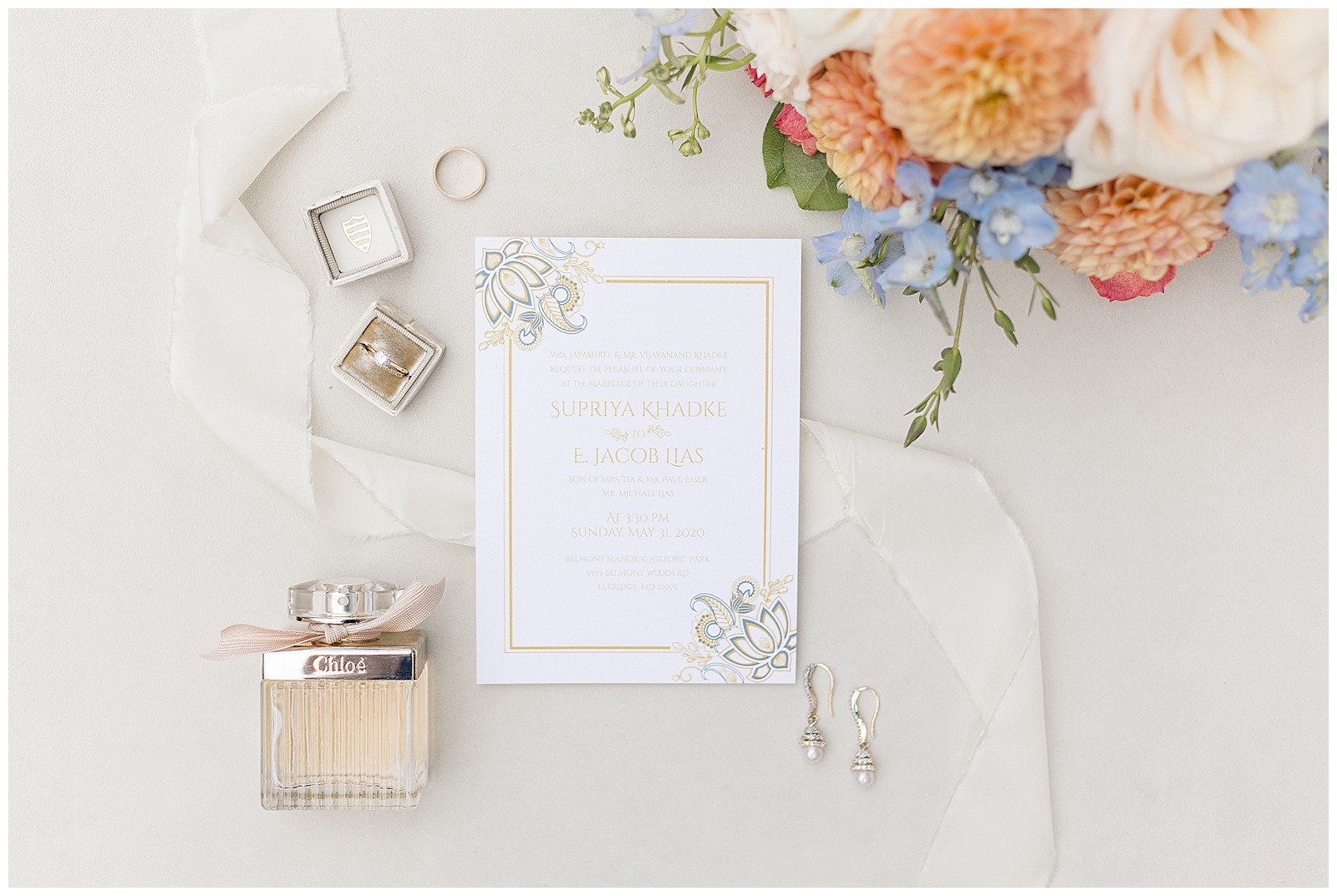 wedding invitation surrounded by vibrant orange and blue flowers and wedding rings and perfume bottle