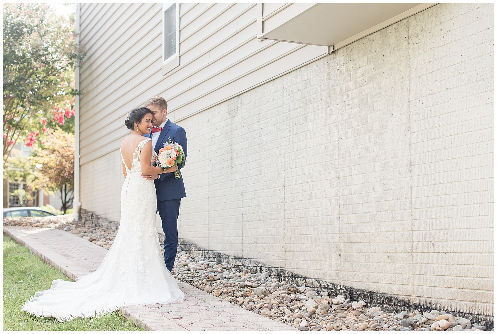 bride in white gown hugging groom in navy blue suit with pink bow tie along stone pathway in ellicott city maryland