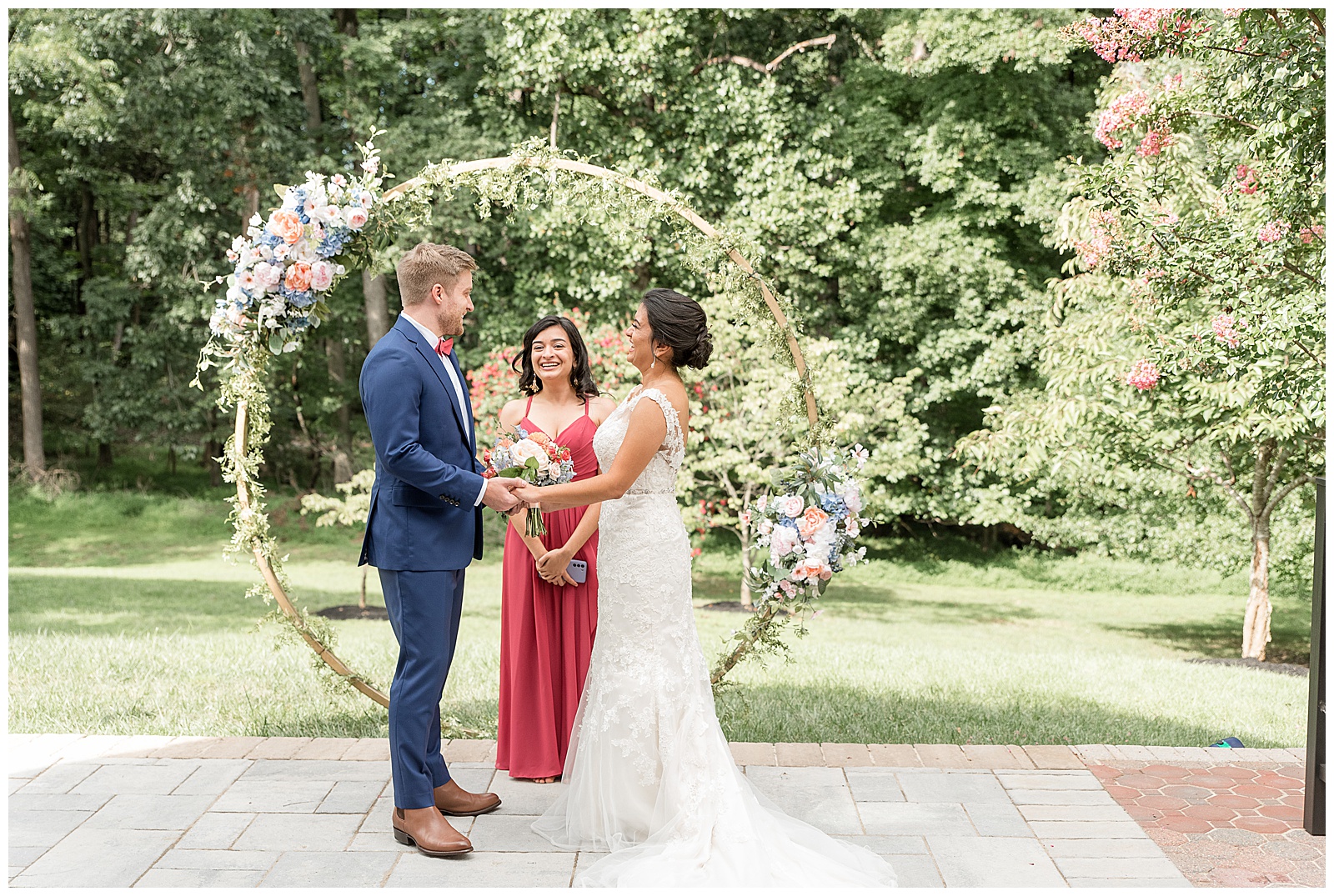 bride and groom facing each other holding hands by beautiful modern floral circular archway as they share wedding vows in ellicott city maryland