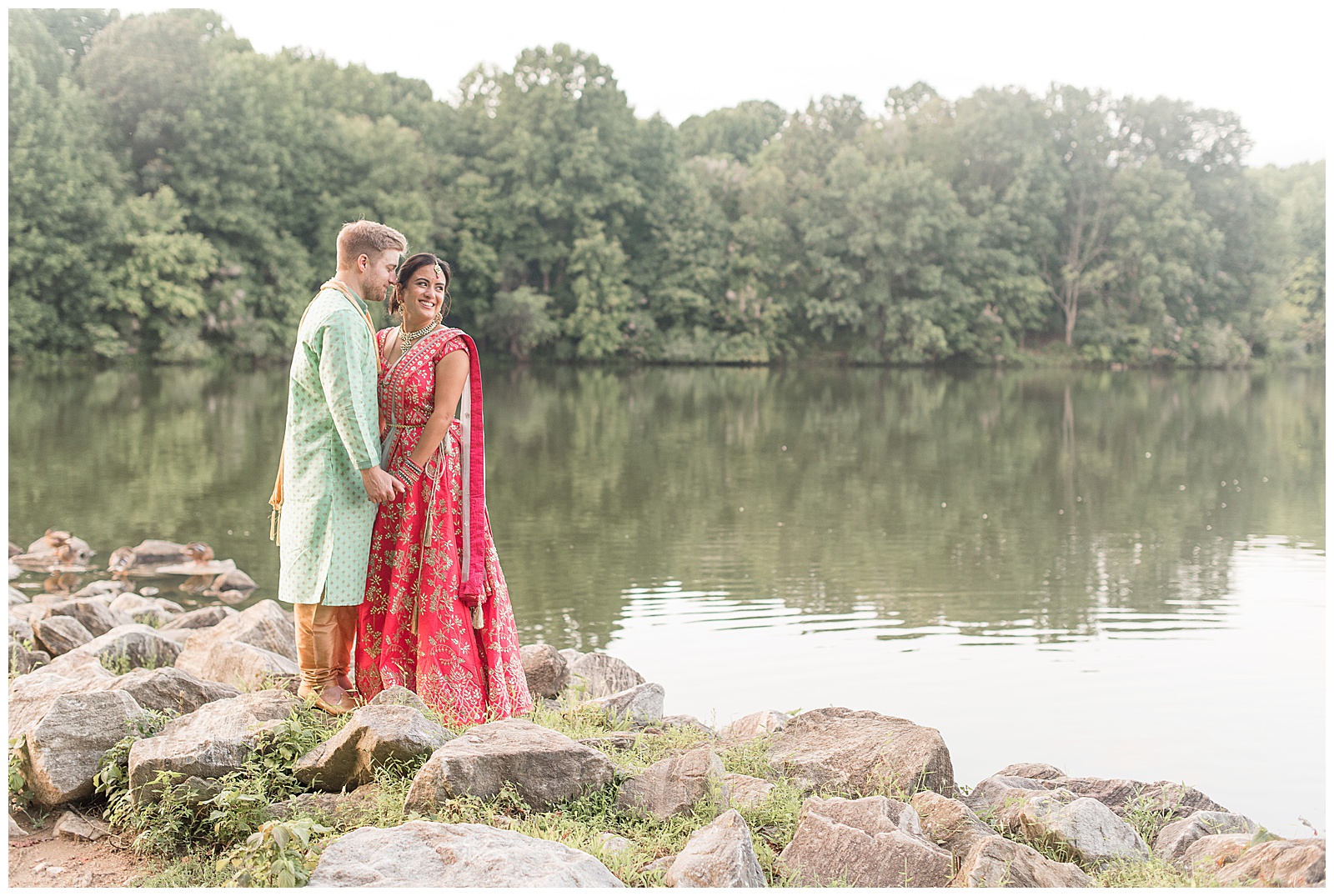 bride and groom hold hands as bride looks over her left shoulder as they stand on large rocks by pond in maryland