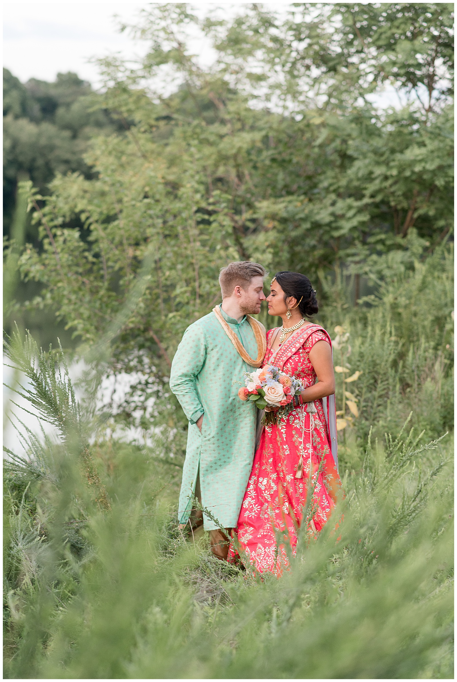 bride and groom stand close almost kissing among bushes and trees beside pond in maryland