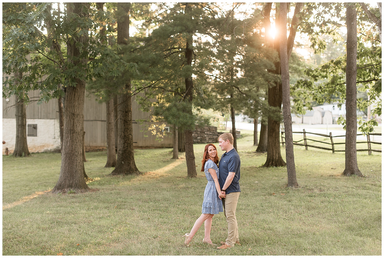 couple holds hand as girl looks at camera and guy looks at girl as the sun peeks through trees in ephrata pennsylvania