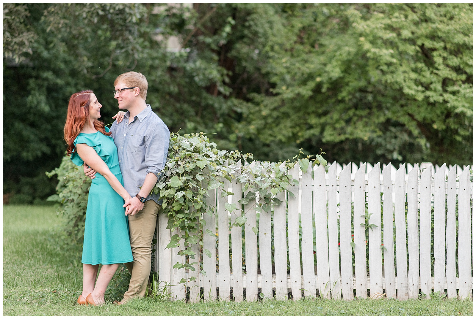 couple hugging by ivy-covered picket fence with girl in teal dress and guy in button up shirt and khaki pants in ephrata