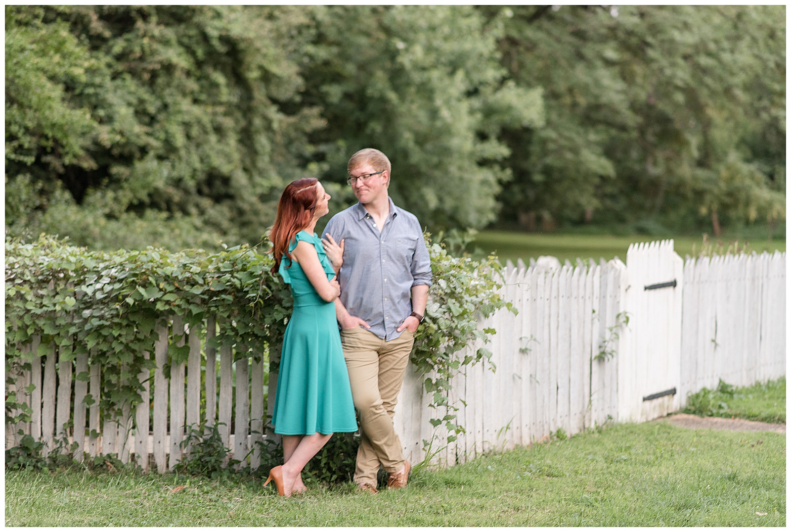 couple standing along picket fence with girl wrapping arms around guy's right arm as they smile at ephrata cloister