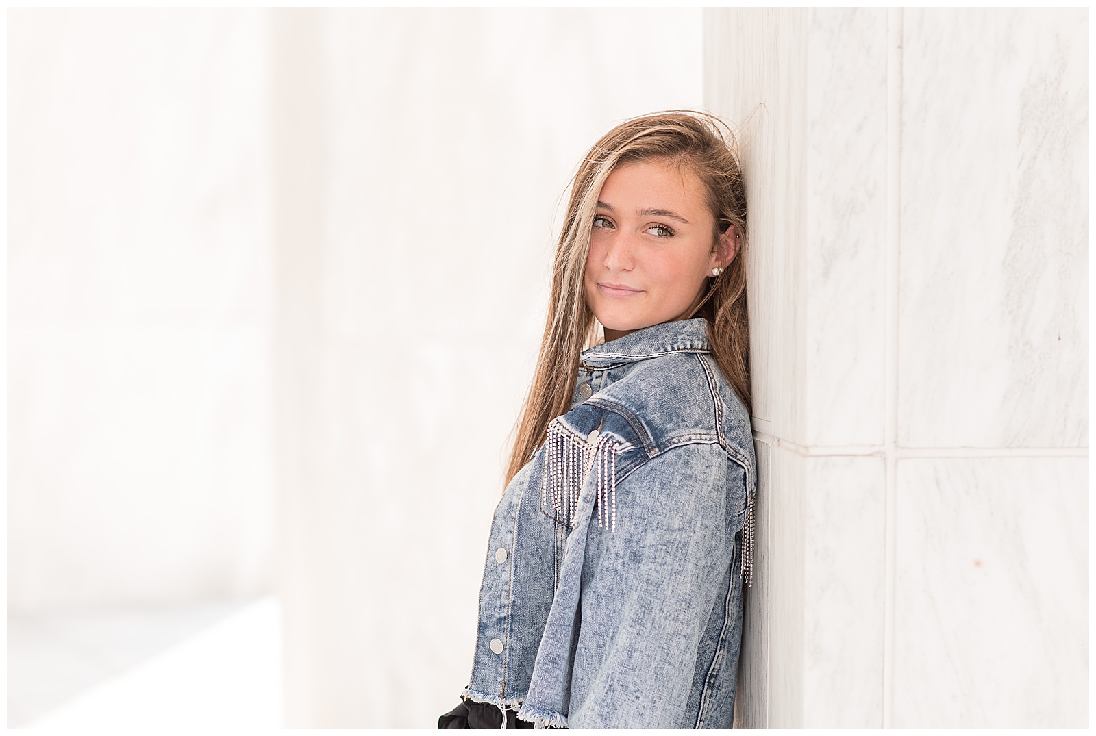 senior girl in blue jean jacket with her back against white column at founders hall in hershey pennsylvania