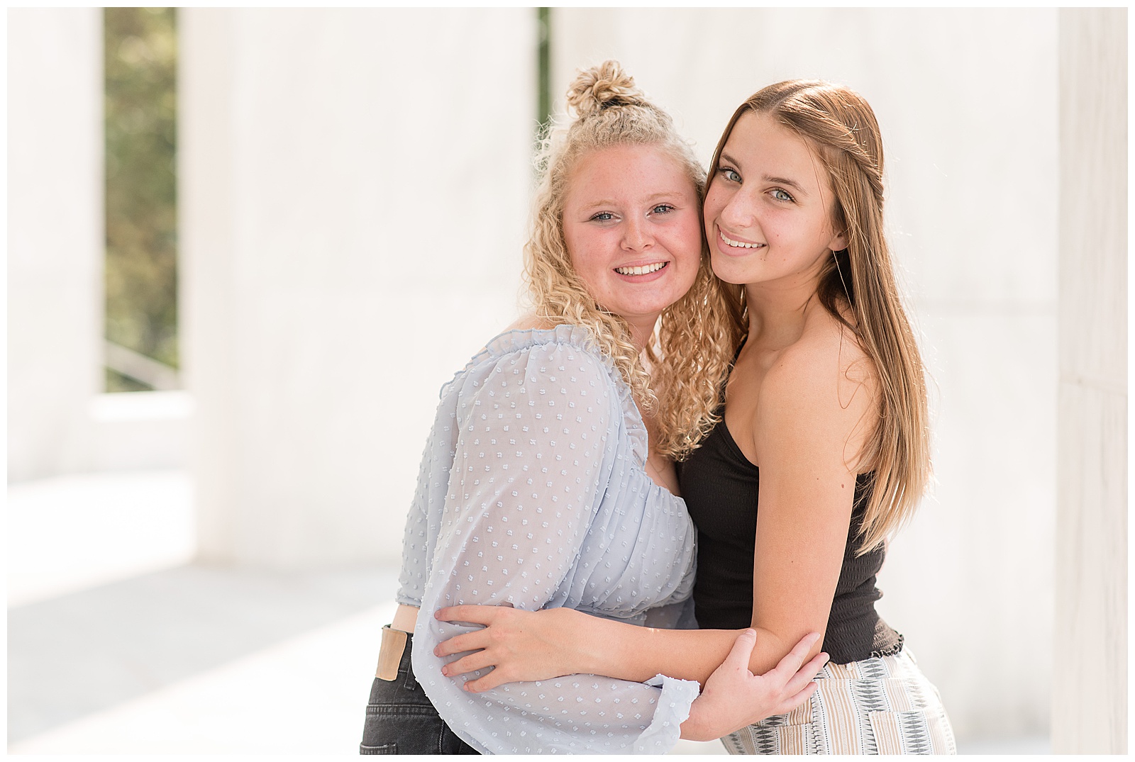 two senior girls hugging with their cheeks pressed together as they smile at founders hall
