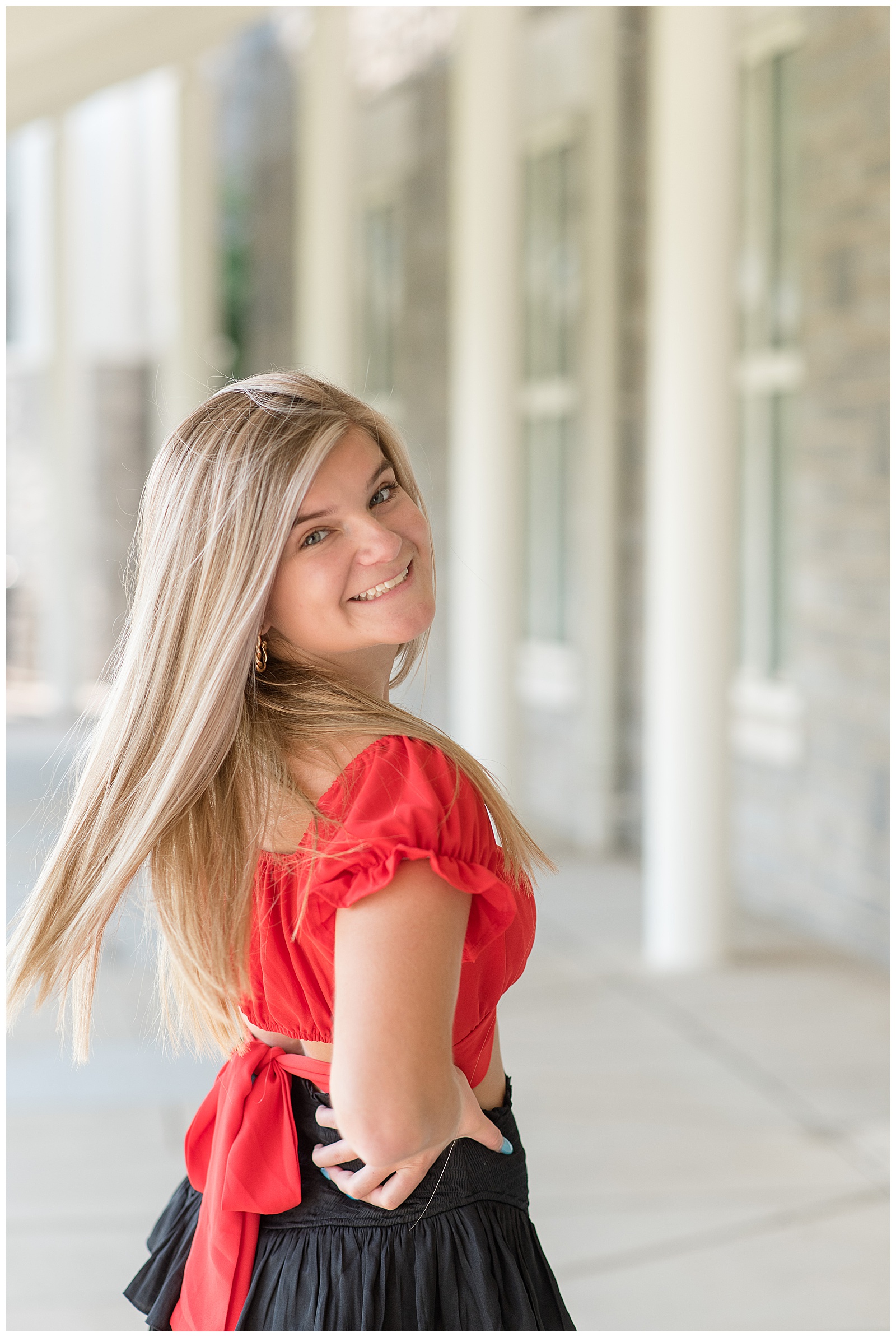 senior girl wearing red shirt spinning around for the camera and smiling with founders hall behind her in hershey pennsylvania