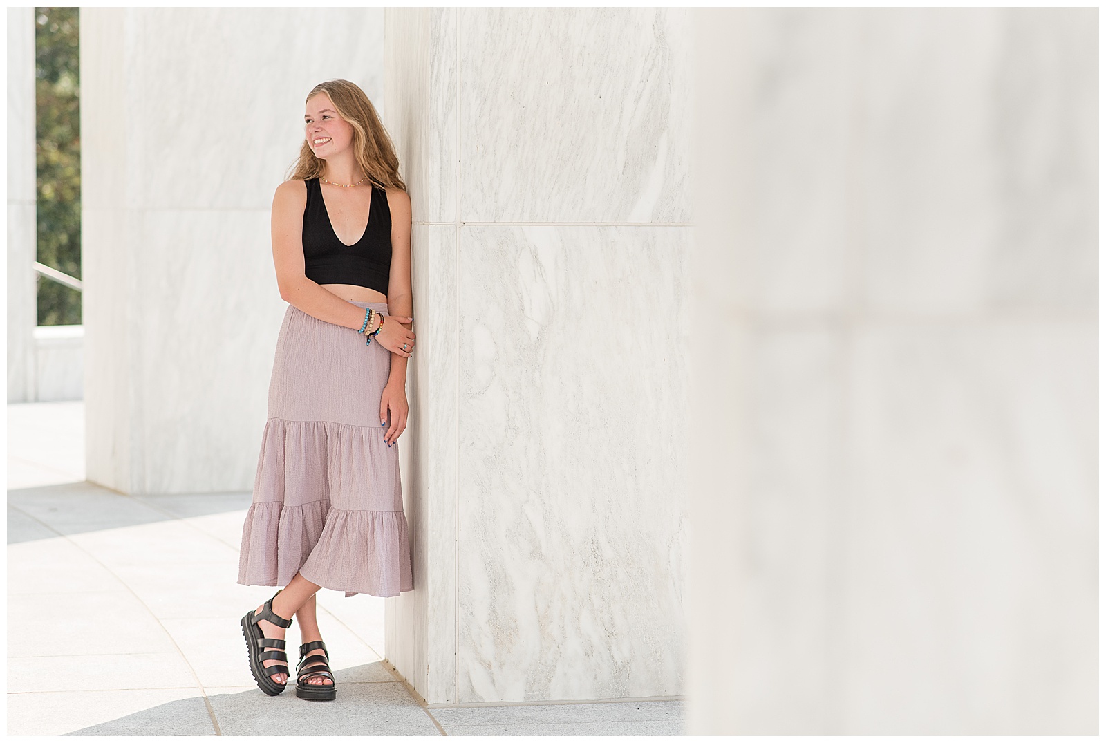 senior girl in black tank top and long skirt leaning left shoulder against wall as she looks right and smiles at founders hall