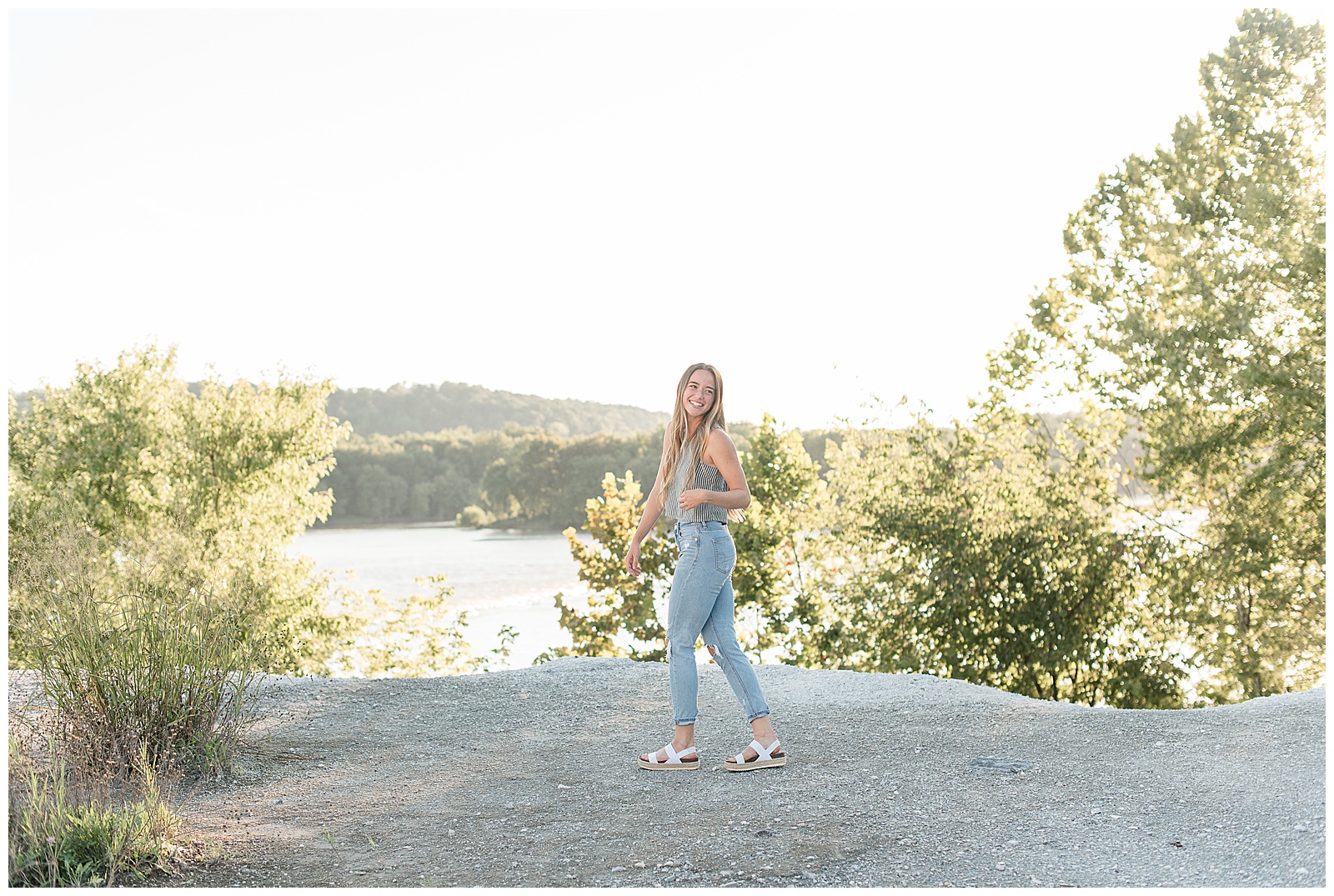senior girl walking along white cliffs of canoy looking over left shoulder and smiling on bright summer evening in lancaster pennsylvania