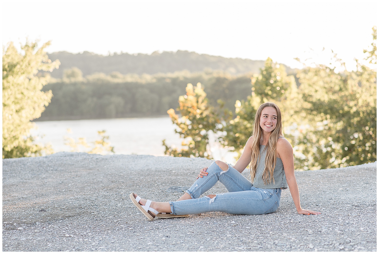 senior girl sitting on large rock with right knee bent and right hand on knee as she smiles and looks over left shoulder in lancaster pennsylvania