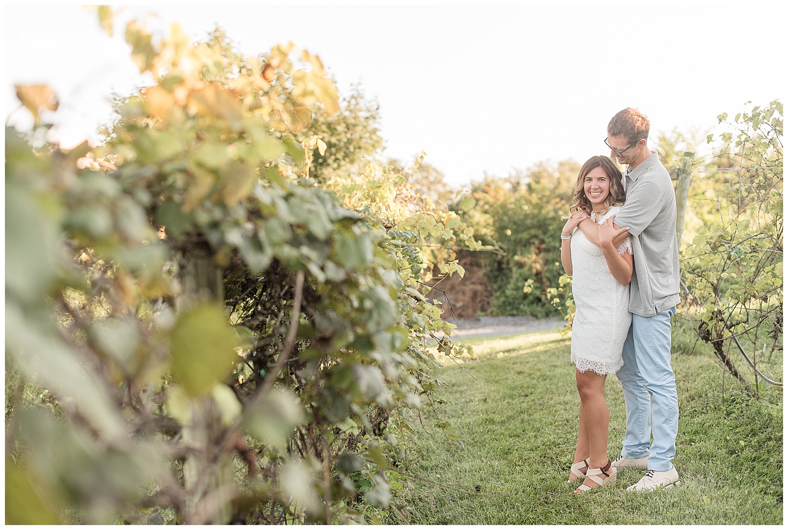 guy hugging girl from behind and looking at her as she smiles at camera on sunny evening at the vineyards at hershey