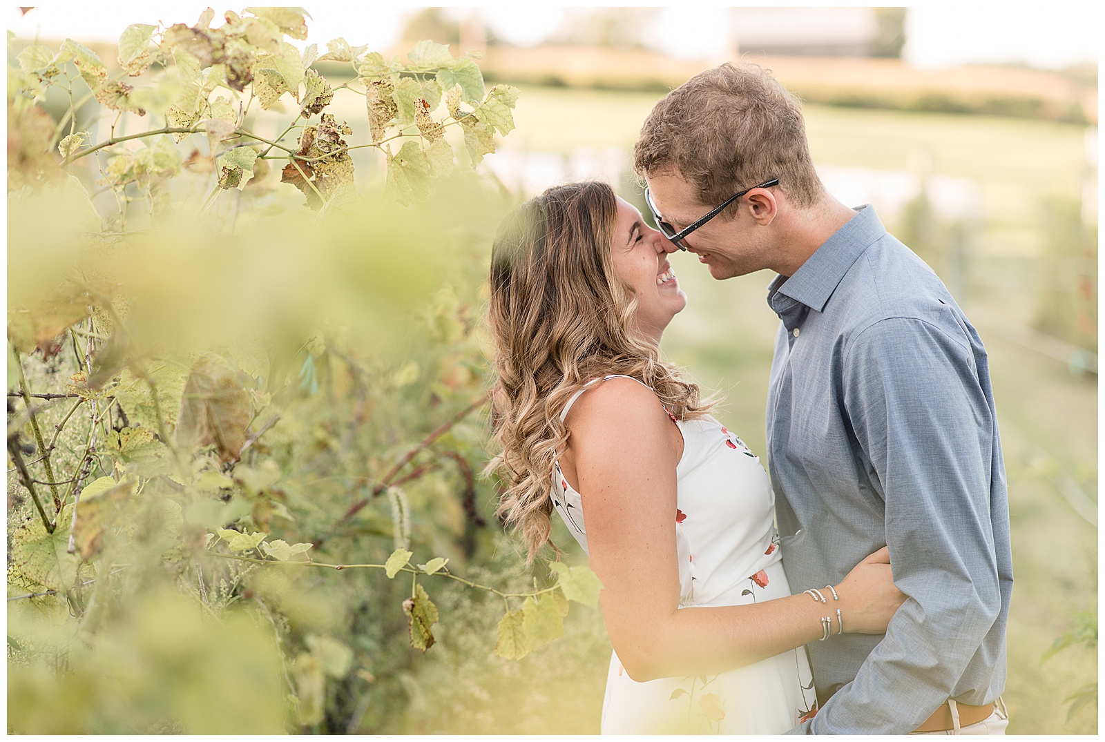 engaged couple smiling and almost kissing as she slightly leans back holding his shirt beside vineyards in hershey pennsylvania