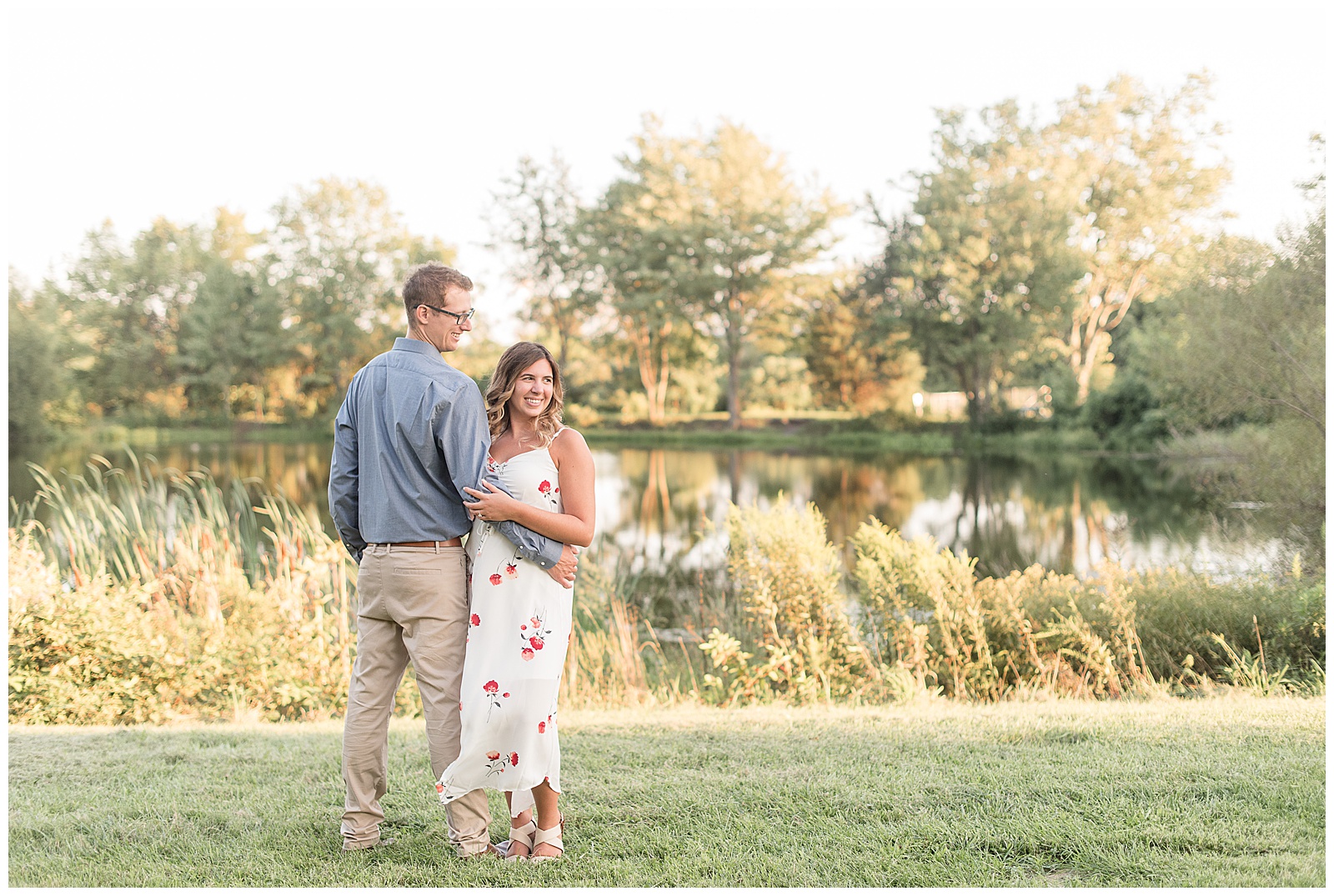 guy's back to camera and girl facing camera with his arm around her waist and their both looking off into the distance with pond and wild grasses and sun setting in hershey pennsylvania