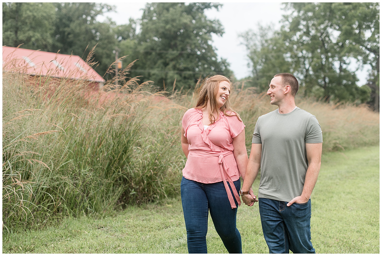 engaged couple walking holding hands and looking at each other smiling by tall grasses at hibernia park