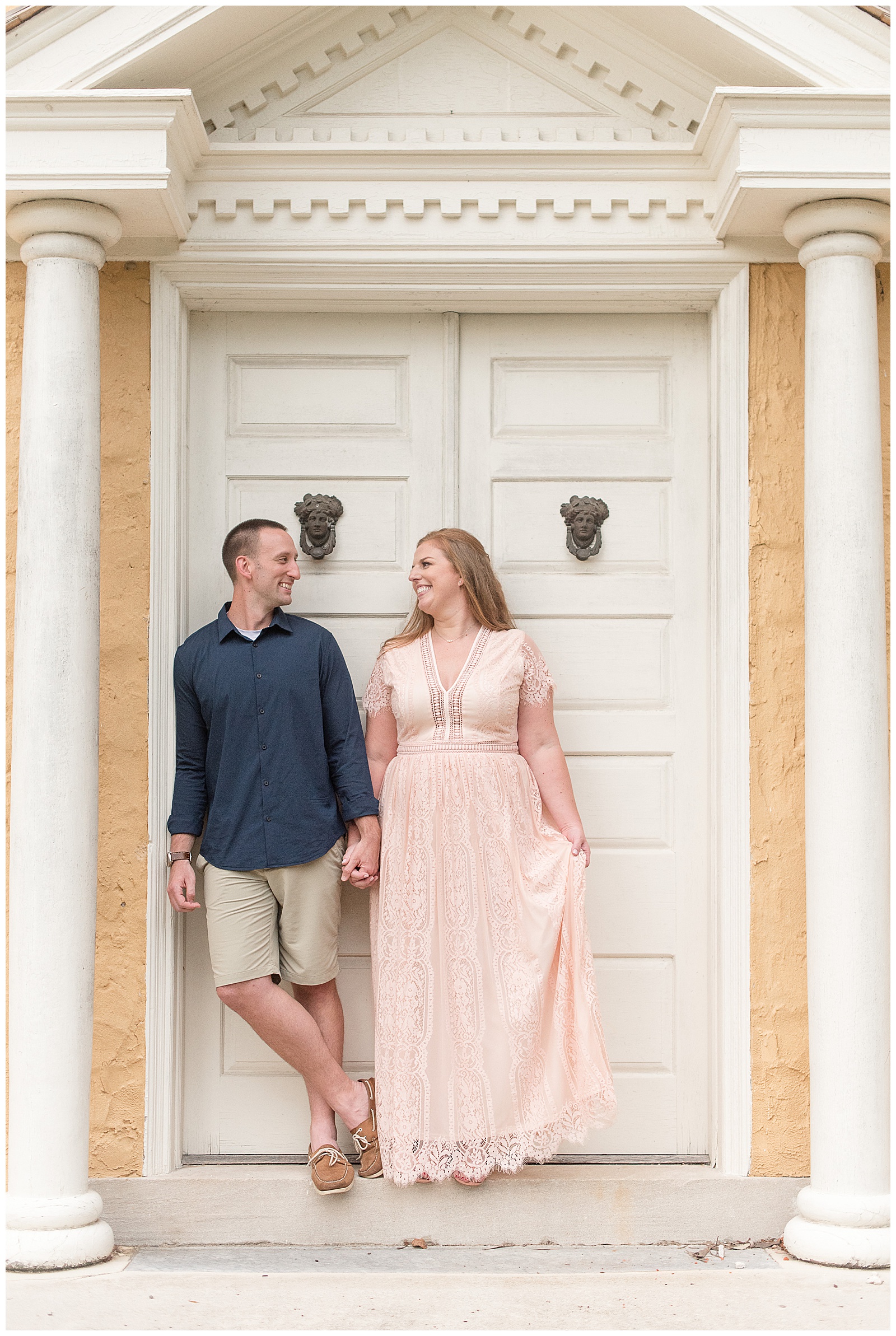 engaged couple holding hands and looking at each other smiling standing in white doorway of historic home at hibernia county park