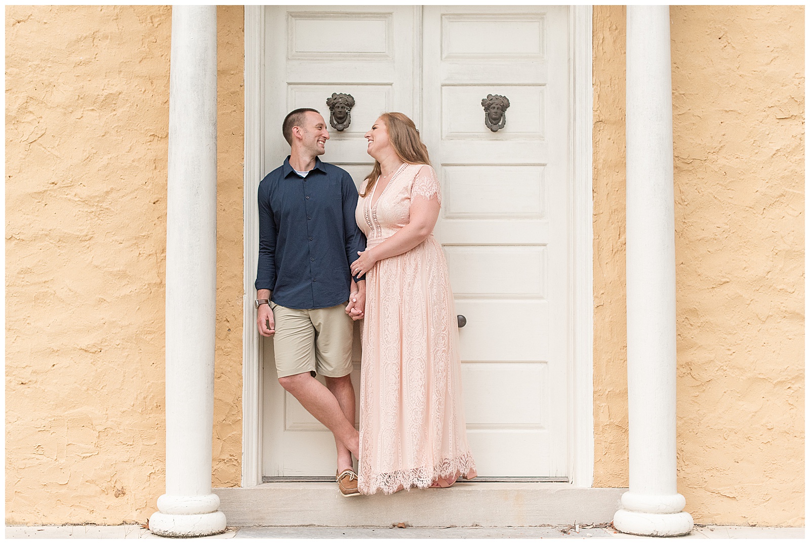 engaged couple standing close smiling against white double doors and white columns at hibernia county park