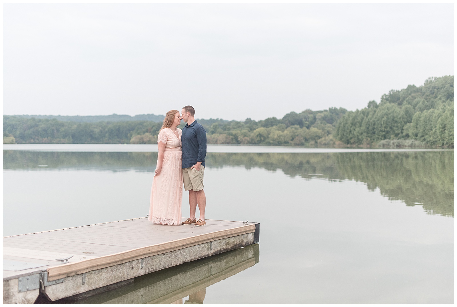 engaged couple almost kissing at edge of dock overlooking lake on cloudy day at hibernia county park