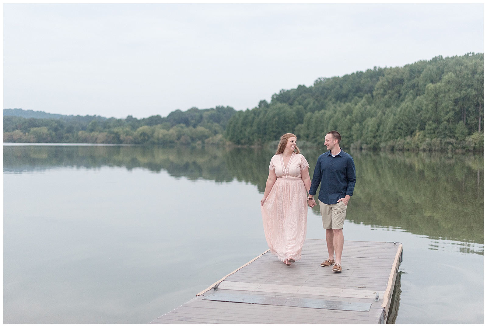 engaged couple holding hands walking on dock towards camera by lake in chester county pennsylvania
