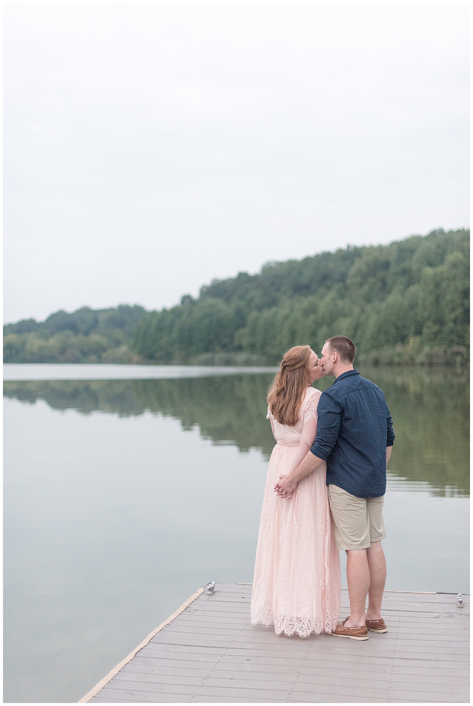 couple kissing with their backs toward camera and his left arm around her on dock by lake at hibernia park